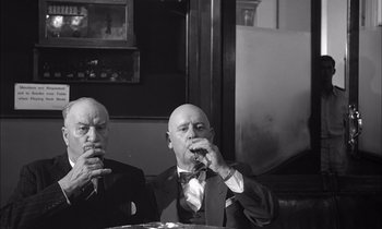 Movie still from “On the Beach” (1959), directed by Stanley Kramer – Two men are sitting at a table and one of them is smoking a cigarette; Medium shot, Low angle