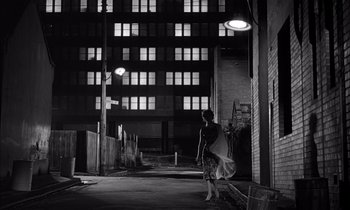 Movie still from “On the Beach” (1959), directed by Stanley Kramer – A woman walking down a street at night with a surfboard; Extreme Wide shot, Low angle