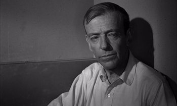Movie still from “On the Beach” (1959), directed by Stanley Kramer – An older man sitting on a bench in front of a wall; Close Up shot, High angle