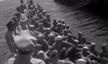 Movie still from “On the Beach” (1959), directed by Stanley Kramer – A black and white photo of a group of men sitting on a boat; Wide shot, High angle