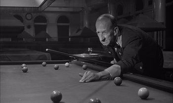 Movie still from “On the Beach” (1959), directed by Stanley Kramer – An older man leaning over a pool table to play a game of billiards; Medium shot, High angle