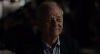 Movie still from “On the Rocks” (2020), directed by Sofia Coppola – An older man in a black jacket smiling; Close Up shot, Over the shoulder angle
