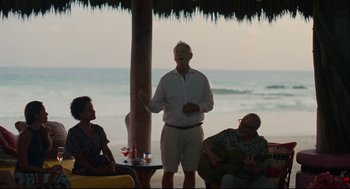 Movie still from “On the Rocks” (2020), directed by Sofia Coppola – An older man standing in front of a group of people; Wide shot, Over the shoulder angle