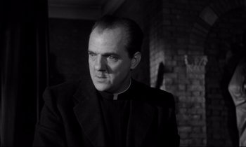 Movie still from “On the Waterfront” (1954), directed by Elia Kazan – A man wearing a priest's outfit and a black jacket; Close Up shot, Low angle