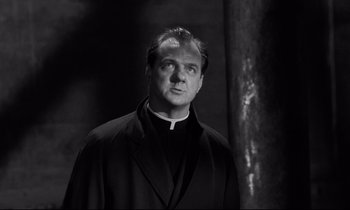 Movie still from “On the Waterfront” (1954), directed by Elia Kazan – A man wearing a priest's outfit standing next to a tree; Close Up shot, Low angle
