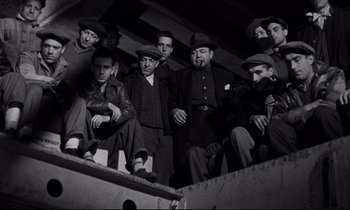 Movie still from “On the Waterfront” (1954), directed by Elia Kazan – A black and white photo of a group of men sitting on a platform; Medium shot, Low angle