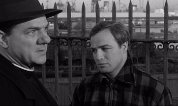 Movie still from “On the Waterfront” (1954), directed by Elia Kazan – Two men standing next to each other in front of a fence; Close Up shot, Over the shoulder angle