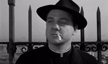 Movie still from “On the Waterfront” (1954), directed by Elia Kazan – A priest smoking a cigarette while wearing a hat; Close Up shot, Low angle