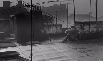 Movie still from “On the Waterfront” (1954), directed by Elia Kazan – A man sitting on the side of a building on top of a skateboard; Wide shot, Overhead angle