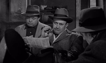 Movie still from “On the Waterfront” (1954), directed by Elia Kazan – A couple of men wearing hats looking at papers; Medium shot, Low angle