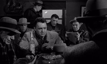 Movie still from “On the Waterfront” (1954), directed by Elia Kazan – A group of men sitting at a table with a bottle; Medium shot, Over the shoulder angle
