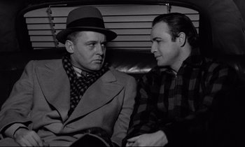 Movie still from “On the Waterfront” (1954), directed by Elia Kazan – Two men sitting next to each other on a couch; Medium shot, Over the shoulder angle