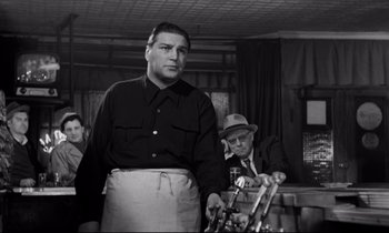 Movie still from “On the Waterfront” (1954), directed by Elia Kazan – A man standing next to another man in a room; Medium shot, Low angle