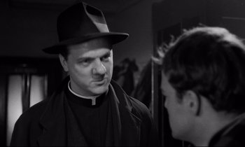 Movie still from “On the Waterfront” (1954), directed by Elia Kazan – A man wearing a hat and a priest's outfit; Close Up shot, Over the shoulder angle