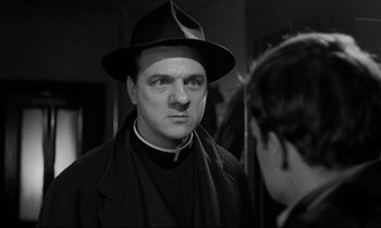 Movie still from “On the Waterfront” (1954), directed by Elia Kazan – A man wearing a hat and a priest's outfit; Close Up shot, Low angle