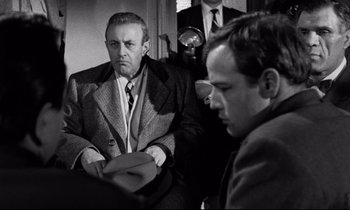 Movie still from “On the Waterfront” (1954), directed by Elia Kazan – A man sitting next to another man in a room; Medium shot, Over the shoulder angle