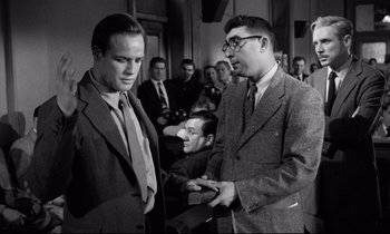Movie still from “On the Waterfront” (1954), directed by Elia Kazan – Two men in suits are standing next to each other in a room; Medium shot, Over the shoulder angle