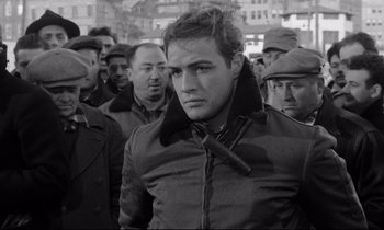 Movie still from “On the Waterfront” (1954), directed by Elia Kazan – Black and white photograph of a man in a crowd; Medium shot, Over the shoulder angle