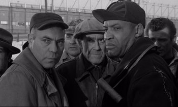 Movie still from “On the Waterfront” (1954), directed by Elia Kazan – A black and white photo of a group of men standing next to each other; Medium shot, Low angle