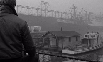 Movie still from “On the Waterfront” (1954), directed by Elia Kazan – A boat is docked in a harbor on a foggy day; Wide shot, Low angle