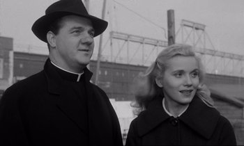 Movie still from “On the Waterfront” (1954), directed by Elia Kazan – A man and a woman standing next to each other in front of a bridge; Medium shot, Low angle