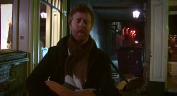 Movie still from “Once” (2007), directed by John Carney – A man sitting down while holding a guitar in his hands; Medium shot, Over the shoulder angle