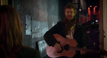 Movie still from “Once” (2007), directed by John Carney – A man with a beard is holding a guitar; Medium shot, Over the shoulder angle