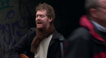 Movie still from “Once” (2007), directed by John Carney – A man wearing a scarf and a jacket is singing; Close Up shot, Low angle