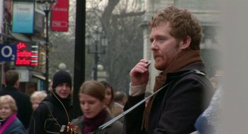 Movie still from “Once” (2007), directed by John Carney – A man smoking a cigarette while standing next to other people; Close Up shot, Over the shoulder angle