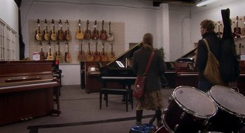 Movie still from “Once” (2007), directed by John Carney – A woman is standing in front of a bunch of musical instruments; Wide shot, High angle