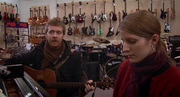Movie still from “Once” (2007), directed by John Carney – A man and a woman playing a guitar in a music store; Medium shot, Over the shoulder angle