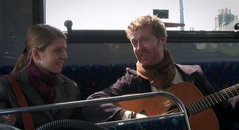 Movie still from “Once” (2007), directed by John Carney – A man sitting next to a woman holding a guitar; Medium shot, Over the shoulder angle