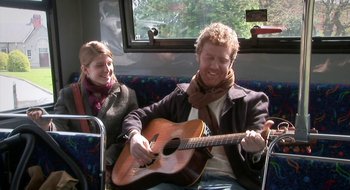 Movie still from “Once” (2007), directed by John Carney – A man and a woman sitting on a bus with a guitar; Medium shot, Over the shoulder angle