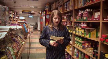 Movie still from “Once” (2007), directed by John Carney – A woman standing in front of a store holding a book; Medium shot, Over the shoulder angle