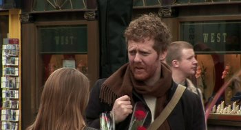 Movie still from “Once” (2007), directed by John Carney – A man in a brown scarf holding a red rose; Medium shot, Over the shoulder angle