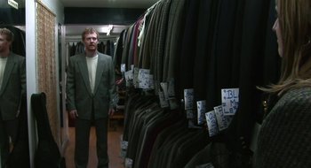 Movie still from “Once” (2007), directed by John Carney – A man standing in front of a room full of suits; Wide shot, Over the shoulder angle