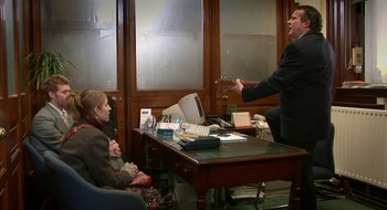Movie still from “Once” (2007), directed by John Carney – A man playing guitar in an office with two women; Wide shot, High angle
