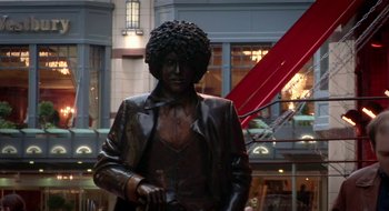 Movie still from “Once” (2007), directed by John Carney – A statue of a man in a suit with a beard; Wide shot, Low angle