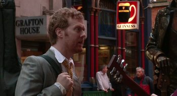 Movie still from “Once” (2007), directed by John Carney – A man in a suit and tie holding a guitar in his hand; Medium shot, Over the shoulder angle