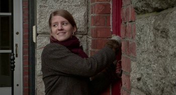 Movie still from “Once” (2007), directed by John Carney – A woman in a plaid jacket and a red scarf is by a brick wall; Close Up shot, Low angle