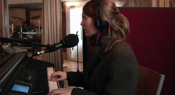 Movie still from “Once” (2007), directed by John Carney – A woman wearing headphones is playing a piano; Medium shot, High angle