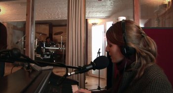 Movie still from “Once” (2007), directed by John Carney – A woman with a microphone is playing a piano; Medium shot, High angle