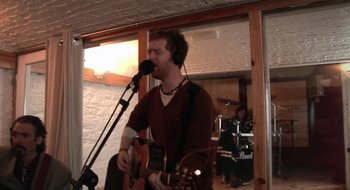 Movie still from “Once” (2007), directed by John Carney – A man with a microphone and a guitar in a room; Medium shot, Low angle