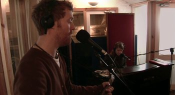 Movie still from “Once” (2007), directed by John Carney – A man and a woman in a recording studio with microphones; Medium shot, Over the shoulder angle
