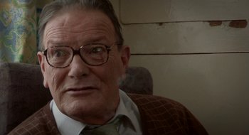 Movie still from “Once” (2007), directed by John Carney – An older man wearing glasses sitting in a chair; Close Up shot, Over the shoulder angle