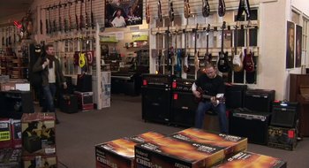 Movie still from “Once” (2007), directed by John Carney – A man sitting in front of an electric guitar in a store; Wide shot, High angle