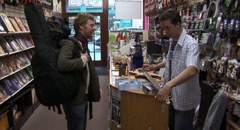 Movie still from “Once” (2007), directed by John Carney – A man standing in front of a man holding a guitar; Wide shot, High angle