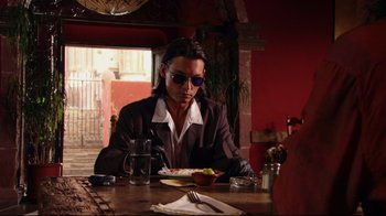 Movie still from “Once Upon a Time in Mexico” (2003), directed by Robert Rodriguez – A man sitting at a table with a plate of food; Medium shot, Low angle