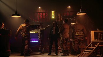 Movie still from “Once Upon a Time in Mexico” (2003), directed by Robert Rodriguez – A group of men standing in a room with a gun; Wide shot, Over the shoulder angle