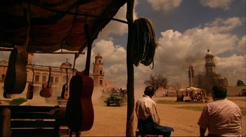 Movie still from “Once Upon a Time in Mexico” (2003), directed by Robert Rodriguez – A man sitting on a chair in a dirt field; Wide shot, Low angle